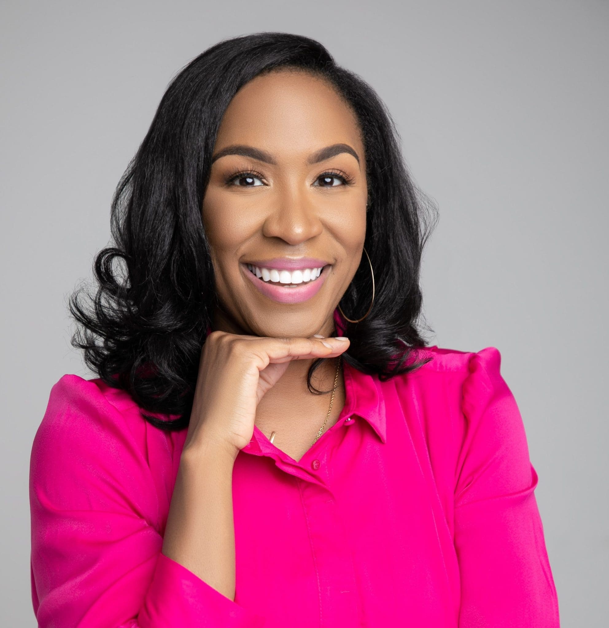 Confident woman in pink shirt, smiling and gesturing, representing professional image and leadership.