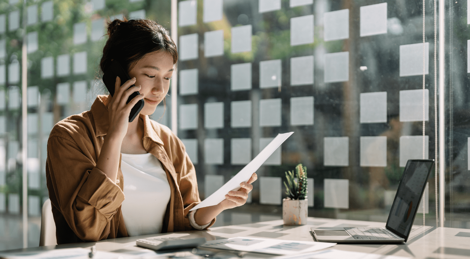 Woman on phone reviewing document at desk, possibly consulting